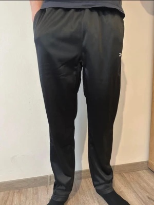 Svarta träningsbyxor från Reebok - Säljer ett par svarta träningsbyxor från Reebok med diskret logga på låret. Byxorna har en avslappnad passform, resår i midjan och är tillverkade i ett lätt och smidigt material som passar perfekt för gym eller löpning.