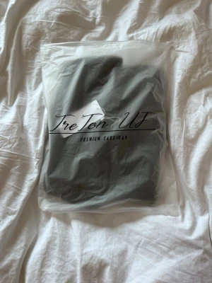 Mörkgrå ribbad cardigan TreTon UF (Pris diskuterbart) - Snygg mörkgrå ribbad cardigan från TreTon UF med dragkedja framtill och hög krage. Tillverkad i ett mjukt stickat material som passar perfekt för lager på lager. Enkel och stilren design som funkar till det mesta.