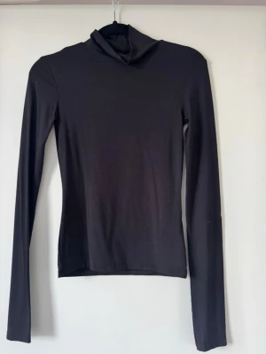 Svart polotopp från Gina Tricot - Säljer en svart polotopp från Gina Tricot i mjukt och stretchigt material. Toppen har lång ärm och en klassisk polokrage, perfekt att styla lager på lager eller bära som den är. Enkel och stilren design som passar till allt.