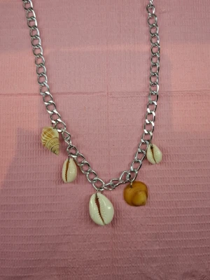Kedjehalsband med snäckor - Snyggt halsband med grov silverfärgad kedja och fem olika snäckor som hängen. Snäckorna är i naturliga toner av vitt, beige och brunt och ger halsbandet en cool strandkänsla. Perfekt accessoar för dig som gillar unika detaljer och boho-vibe.