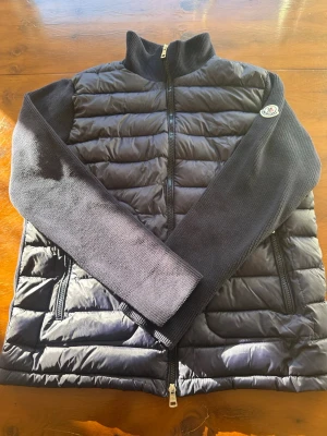 Mörk blå Moncler Cardigan - Snygg blå cardigan från Moncler med stickade ärmar och hög krage. Den har två dragkedjeförsedda fickor och ett Moncler-märke på ena ärmen. Perfekt för lager-på-lager och ger en stilren look.