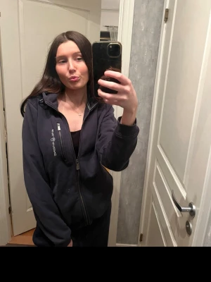 Marinblå hoodie från Sail Racing - Snygg marinblå hoodie från Sail Racing med dragkedja framtill och en praktisk bröstficka med zip. Hoodien har vit logga på bröstet och på huvan. Tillverkad i ett mjukt och bekvämt material, perfekt för chill dagar eller när du vill ha en sportig look. Säljer då den inte kommer till användning. Storlek 170, passar för er som har S-XS. Kom dm om ni är intresserade! 🩷