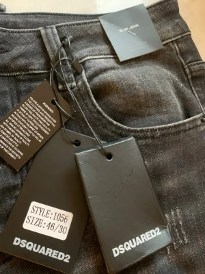 Svarta slim jeans från Dsquared2 - Säljer ett par svarta slim fit jeans från Dsquared2 med slitningar, färgstänk och detaljer som dragkedja och nyckelring. Jeansen har klassisk femficksmodell och är tillverkade i stretchigt denim för skön passform. Perfekta för dig som gillar en edgy streetstil.