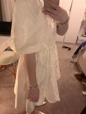 Malina-klänning - Superfin vit kort klänning med puffärmar och lätt glansigt tyg. Klänningen har rund halsringning och markerad midja, vilket ger en söt och trendig siluett. Perfekt för dig som gillar romantiska vibes och vill sticka ut lite extra. Helt ny med prislappen o förpackningen kvar!! Aldrig använd:) strl S