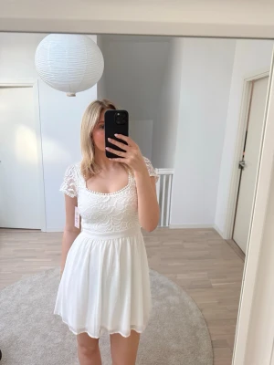 Vit spetsklänning med kort ärm - Helt oanvänd vit kort klänning med spetsdetaljer och korta ärmar. Perfekt till student eller sommarens alla tillfällen. Lappen är kvar. Köparen står för frakt.