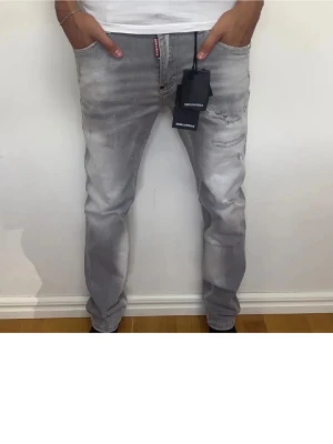 Dsquared2 jeans - Säljer ett par snygga gråa jeans från Dsquared2 med slitningar och tvättad look. Jeansen har rak passform, klassiska fem fickor och tydliga logotaggar fram och bak. Knappast använda Skick: 9/10