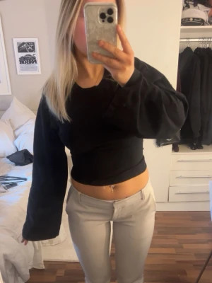 Svart croppad topp med knyt i ryggen - Trendig svart croppad topp med långa, vida ärmar och snygg knytning i ryggen. Toppen har en tight passform i midjan.