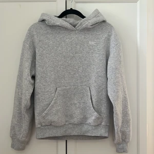 Grå hoodie med NYC-tryck - Säljer en stilren grå hoodie med ett litet 'NYC' tryck på bröstet. Den har en klassisk känguruficka och en bekväm huva. Perfekt för en avslappnad look.