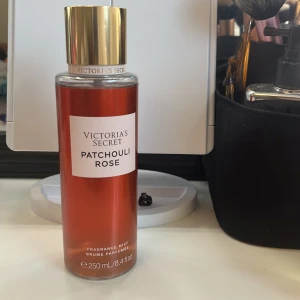 Patchouli Rose Fragrance Mist från Victoria's Secret - En doftmist från Victoria's Secret med en sensuell blandning av patchouli och ros. Flaskan är elegant med en röd ton och har en gyllene kork. Innehåller 250 ml av en blommig och fruktig doft med inslag av persika. Vätskan ä upp till etiketten.