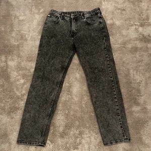 Grå/svarta jeansbyxor från H&M - Snygga svarta jeansbyxor från H&M med en relaxed fit och justerbar midja. Byxorna har en tapered leg och klassisk femficksdesign. Perfekta för en avslappnad stil.