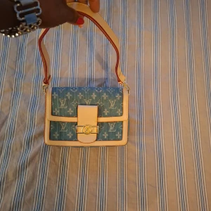 Blå och beige axelväska - Snygg axelväska i blått och beige med monogrammönster. Väskan har en justerbar axelrem och ett elegant spänne framtill. Perfekt för att ge din outfit en touch av stil.