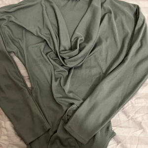 Mörkgrön långärmad topp från Zara - Snygg grön långärmad topp från Zara med draperad halsringning. Perfekt för en stilren look. Materialet känns mjukt och bekvämt mot huden. Som ny, inga deffekter eller skador.Finns även i svart