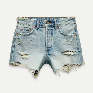 Blå jeansshorts från Zara - Snygga blå jeansshorts från Zara med slitna detaljer och råa kanter. Perfekta för en avslappnad stil. De har en klassisk femficksdesign och knappgylf.