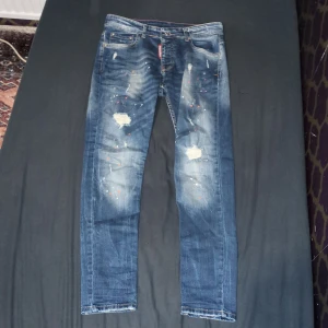 Blå jeans från Dsquared2 - Snygga blå jeans från Dsquared2 med coola slitningar och färgstänk. De har en klassisk femficksdesign och en knappgylf. Perfekta för en avslappnad stil med en touch av edge.