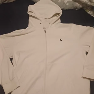 Vit hoodie från Polo Ralph Lauren - Säljer en stilren vit hoodie från Polo Ralph Lauren. Den har en dragkedja framtill och en klassisk logga på bröstet. Perfekt för en avslappnad look. Pris kan diskuteras.