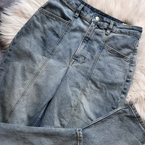 Blå jeans med hög midja - Blå jeans med hög midja och  sömm längs mitten av benet. De har en knapp och dragkedja framtill samt raka ben.