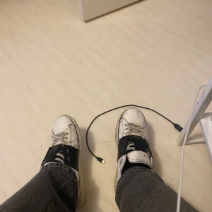 Valentino open - Säljer ett par vita sneakers med svarta detaljer och snörning. Skorna har en klassisk design med en bred svart rem på sidan. Perfekta för en avslappnad stil. Dom är ganska slitna men hål i sulan