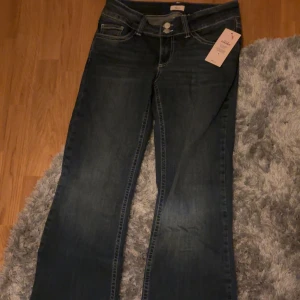 Mörkblå bootcut jeans från Nelly - Snygga mörkblå bootcut jeans från Nelly med låg midja. Jeansen har dekorativa sömmar på bakfickorna och stängs med dragkedja. Fick dessa i julklapp tyvärr var dom lite för stora i midjan och gick ej att returnera för att det gått för lång tid. Stretchiga och bekväma samt bra i längd för mig som är ca 175 cm lång. Aldrig använts och prislappen sitter kvar💕