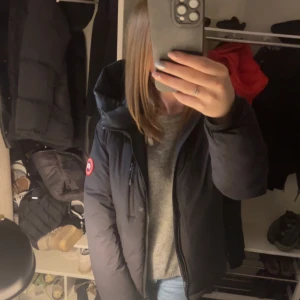 Svart dunjacka från Canada Goose - !Gammal model! Säljer en svart dunjacka från Canada Goose med deras ikoniska märke på ärmen.  Jackan har en dragkedja framtill och är perfekt för kalla dagar. Den är långärmad och har en normal passform. Perfekt för vintern! 