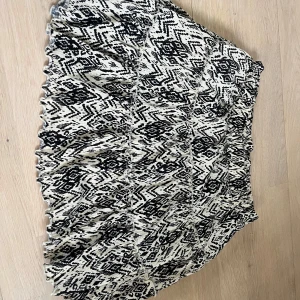 Mönstrad kjol från Lindex - Snygg mönstrad kjol från Lindex i svart och vit. Kjolen har ett elastiskt midjeband för extra komfort och ett trendigt geometriskt mönster. Perfekt för att ge din outfit en unik touch! 