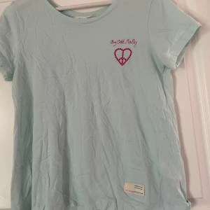 Ljusblå t-shirt från Odd Molly - Säljer en ljusblå t-shirt från Odd Molly med ett mörkrosa hjärtmönster och texten 'By Odd Molly' på bröstet. T-shirten har korta ärmar och en avslappnad passform. Perfekt för en casual look! T-shirten är i fint skick samt sparsamt använd. Vid frågor och funderingar hör av er, jag svarar så fort jag kan!🩷