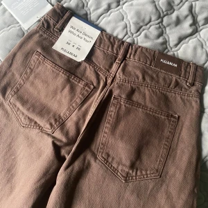 Bruna jeansbyxor från Pull&Bear - Snygga bruna jeansbyxor från Pull&Bear med klassisk femficksdesign. Byxorna har en knapp och dragkedja framtill och är perfekta för en avslappnad stil. De är tillverkade i ett slitstarkt material som ger en bekväm passform.