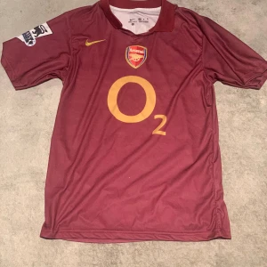 Arsenal tröja 2005/06 - Säljer en vinröd Arsenal fotbollströja från Nike. Tröjan har klubbens emblem och sponsorlogga på framsidan samt 'Henry 14' tryckt på baksidan. 