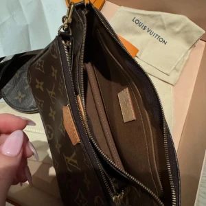 Monogram axelväska från Louis Vuitton - Säljer en snygg axelväska från Louis Vuitton i klassiskt monogrammönster. Väskan har en avtagbar kedja och en justerbar axelrem. Den är perfekt för att bära dina viktigaste saker med stil. Inkluderar även en rund plånbok som matchar väskan.