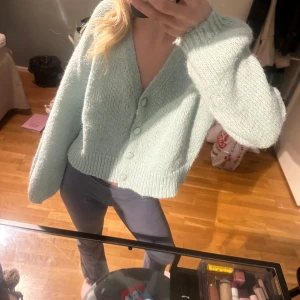 Ljusgrön stickad kofta - Mysig ljusgrön stickad kofta med knappar framtill. Koftan har en croppad passform och långa ärmar, perfekt för en avslappnad stil.