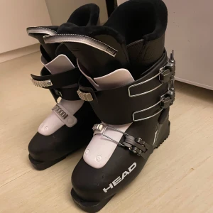 Svarta pjäxor från Head - Säljer ett par svarta pjäxor från Head med justerbara spännen i silver. De har en robust design och är perfekta för vintersport. Insidan är vadderad för extra komfort. Storlek 25,5 (motsvarar ungefär storlek 40). Yttermått är 297 mm.   Väldigt sköna och lätta att ta på/av. Sköna att gå i och ha på en hel dag oså.