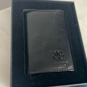 Svart plånbok från Bibtex - Snygg och stilren svart plånbok från Bibtex i skinn. Plånboken har en elegant design med plats för kort och sedlar. Perfekt för den som vill ha en praktisk och klassisk accessoar.