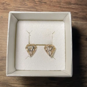 Guldiga örhängen med diamantform - Snygga guldiga örhängen i form av diamanter. Perfekta för att ge en elegant touch till din outfit. Kommer i en fin ask. Från Montini.