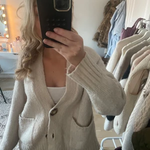 Beige kofta med knappar - Mysig beige kofta med stora knappar och två fickor framtill. Perfekt för kyligare dagar och lätt att matcha med olika outfits.