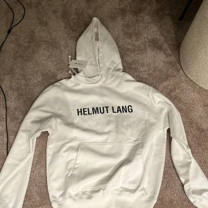 Vit hoodie från Helmut Lang - Säljer en stilren vit hoodie från Helmut Lang med svart text på framsidan. Den är i storlek M och helt oanvänd tagen sitter fortfarande på