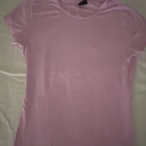 Ljusrosa t-shirt från Gina Tricot - Säljer en ljusrosa t-shirt från Gina Tricot i storlek XS. Den har en klassisk rund hals och korta ärmar, perfekt för en avslappnad stil. T-shirten är gjord i ett mjukt och bekvämt material.