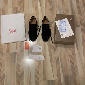 Svarta sneakers från Christian Louboutin - Snygga svarta sneakers från Christian Louboutin med den ikoniska röda sulan. Skorna har snörning och är tillverkade i ett elegant material som ger en lyxig känsla. Perfekta för den som vill ha stil och komfort i ett.
