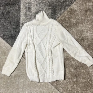 Vit stickad tröja - Säljer en stilren vit stickad polotröja med ett snyggt flätmönster på framsidan. Tröjan har långa ärmar och en hög polokrage som håller dig varm under kyliga dagar. Perfekt för både vardag och mer uppklädda tillfällen.