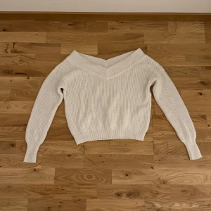 Vit stickad offshoulder tröja - Säljer en stilren vit stickad tröja med offshoulder-design. Tröjan har långa ärmar och en ribbad struktur som ger en snygg passform. Perfekt för kyligare dagar och att matcha med dina favoritjeans.