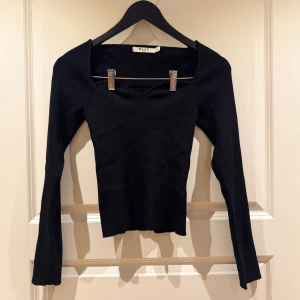 Svart ribbad topp från NA-KD - Snygg svart ribbad topp från NA-KD med långärmad design och fyrkantig halsringning. Perfekt för en stilren look. Passar bra till både jeans och kjol.