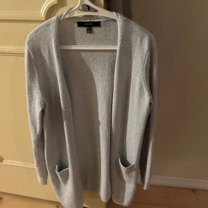 Ljusgrå kofta från Vero Moda - Säljer en stilren ljusgrå kofta från Vero Moda. Den har en öppen design med långa ärmar och praktiska fickor framtill. Perfekt för lager-på-lager under kyligare dagar.
