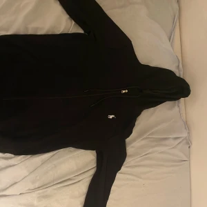 Svart huvtröja med dragkedja - Snygg svart huvtröja med dragkedja och en liten polo logga på bröstet. Perfekt för en avslappnad stil. Tröjan har långa ärmar och en praktisk huva.