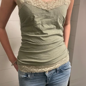 Olivgrön linnetopp med spetsdetaljer - Snygg olivgrön linnetopp med vackra spetsdetaljer vid halsringning och nederkant. Toppen är ärmlös och har en tight passform, perfekt för sommardagar.Den är också väldigt fin och bekväm för både skolan och fester💞💞