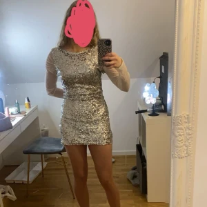Glittrig klänning från These Little Words - Klänningen är i storlek L men den passar på mig som är S. Snygg glittrig klänning i silver med långa ärmar och öppen rygg. Perfekt för en festlig kväll när du vill glänsa lite extra. Klänningen har en tight passform och är kort i modellen. 💕
