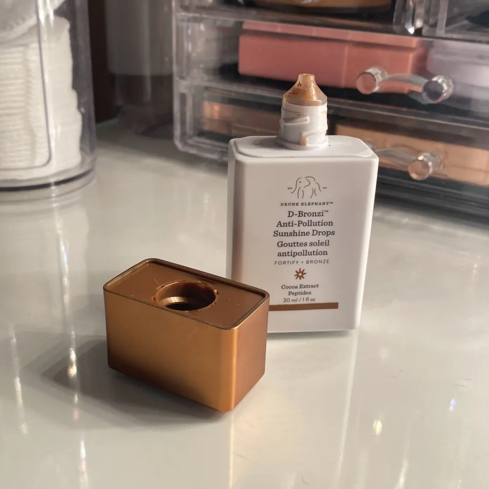 D-Bronzi Anti-Pollution Sunshine Drops från Drunk Elephant ger en solkysst look med ett skydd mot föroreningar. Kommer i en praktisk flaska med bronsfärgat lock. Perfekt för att blanda med din dagkräm eller foundation för extra lyster.. Beauty.