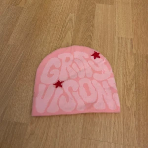 Rosa mössa med text och stjärnor - Cool rosa mössa med texten 'GRAVITY VISION' och röda stjärnor på framsidan. Baksidan har ett spindelnätsmönster. Perfekt för att sticka ut i mängden!