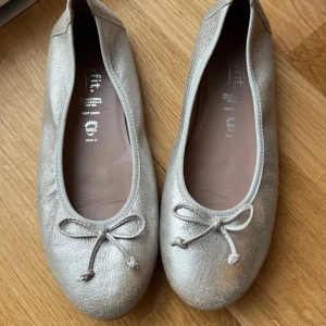Silvriga ballerinaskor från Superfit - Snygga silvriga ballerinaskor från Superfit (fint märke) med rosett. Använda några få gånger. Jättefint skick.