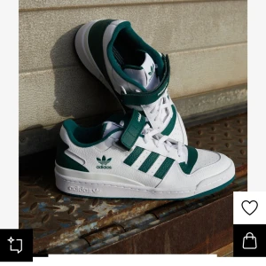 Adidas sneakers i vitt och grönt - Snygga Adidas sneakers i vitt med gröna detaljer och klassiska tre ränder. Skorna har snörning och kardborreband för extra stöd. Perfekta för en sportig look. Använda ca 