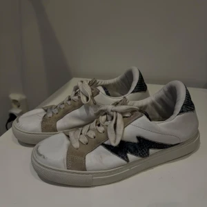 Zadig & Voltaire sneakers  - Snygga vita sneakers med en cool blixtdetalj i mörkblått mönster. Skorna har beige mockadetaljer. Från Zadig&Voltaire. Storlek 40. Lite skavna, se bild 