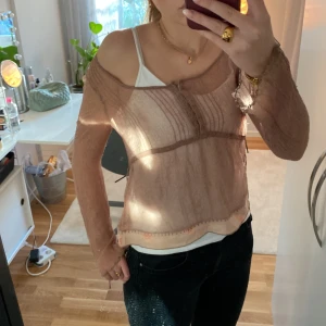 Beige transparent blus från Noa Noa (kontakta mig innan köp) - Säljer en elegant beige transparent blus från Noa Noa. Blusen har en v-ringad design och långa ärmar, perfekt för lager-på-lager-stil. Den är lätt och luftig, vilket gör den idealisk för varmare dagar.