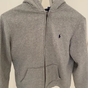 Grå hoodie från Ralph Lauren - Säljer denna Ralph lauren zip i en grå färg, som är i ett mycket bra skick med enstaka defekt (skick: 8,5-10). Storleken är 14-16 i barn, som är ungefär som xs i vuxenstorlek. Nypris runt 1500. Hör av dig vid minsta fundering. Priset är ej fast!